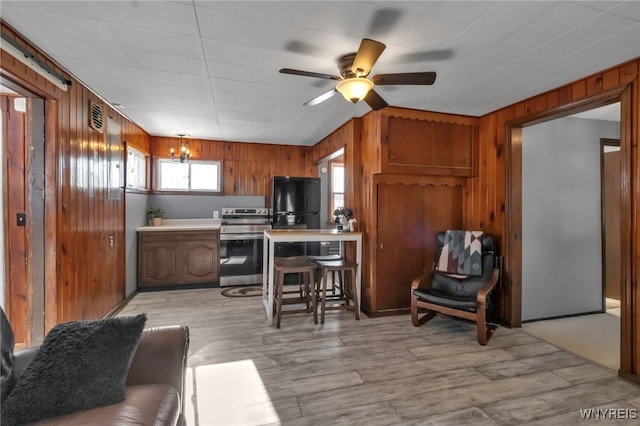 kitchen with wooden walls, ceiling fan with notable chandelier, black fridge, and stainless steel range with electric cooktop