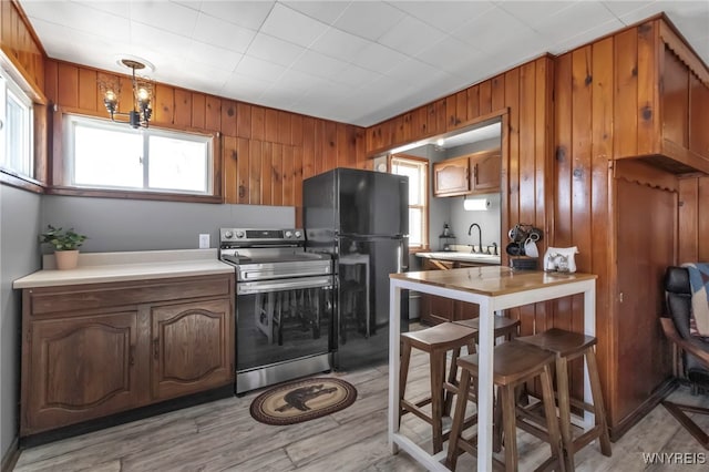 kitchen featuring black refrigerator, a wealth of natural light, decorative light fixtures, electric range, and light hardwood / wood-style flooring