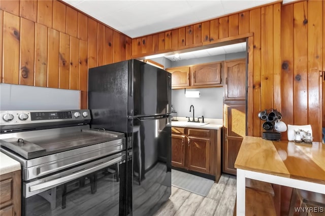 kitchen featuring black refrigerator, sink, wood walls, light wood-type flooring, and stainless steel electric range