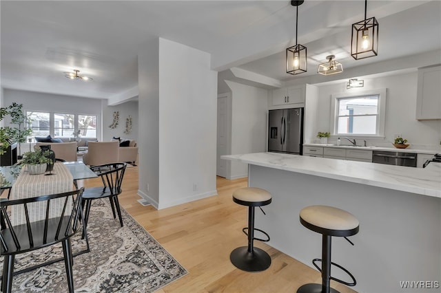 kitchen with hanging light fixtures, sink, white cabinets, light stone counters, and stainless steel appliances