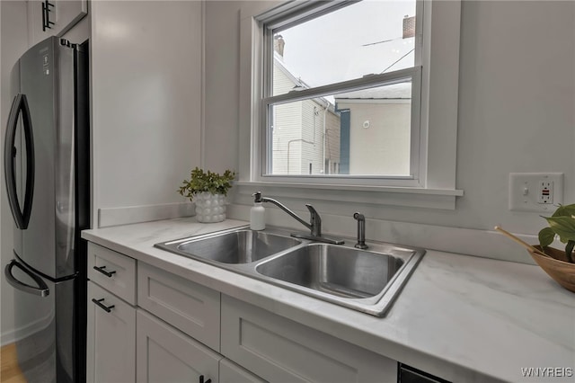 kitchen featuring light stone counters, sink, white cabinetry, and black fridge