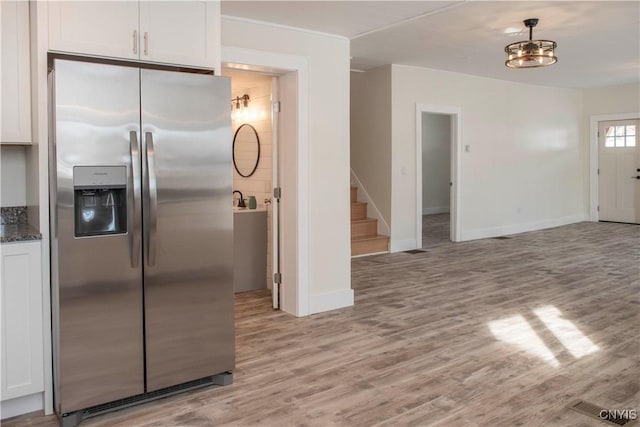 kitchen with dark stone countertops, light wood-style flooring, stainless steel refrigerator with ice dispenser, and white cabinets