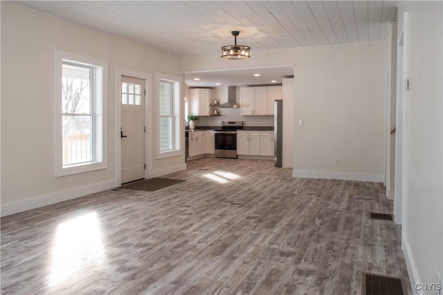 kitchen featuring dark countertops, wall chimney range hood, open floor plan, wood finished floors, and stainless steel appliances