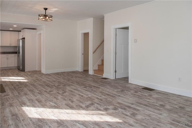 unfurnished living room featuring light wood finished floors, stairway, baseboards, and visible vents