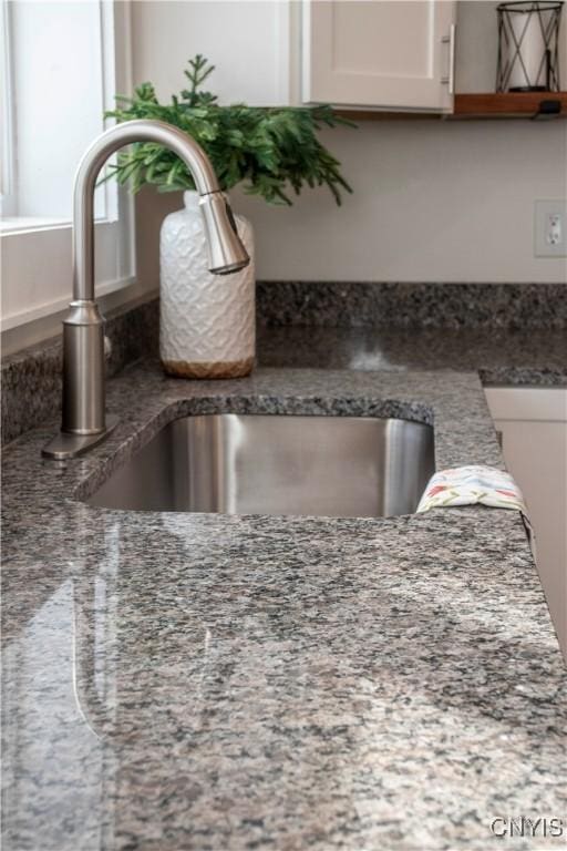 room details with white cabinetry, dark stone counters, and a sink