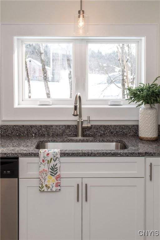 kitchen with a sink, stainless steel dishwasher, white cabinets, and dark stone countertops