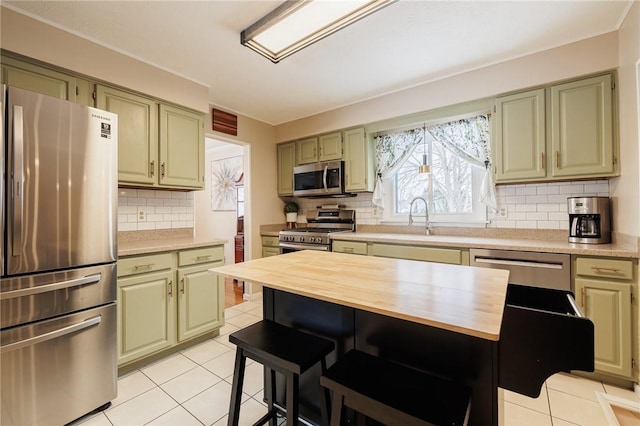 kitchen featuring appliances with stainless steel finishes, sink, tasteful backsplash, light tile patterned floors, and green cabinetry