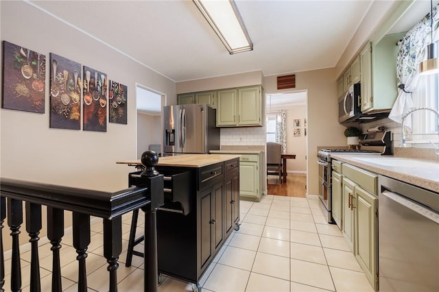 kitchen featuring green cabinets, sink, backsplash, light tile patterned floors, and stainless steel appliances