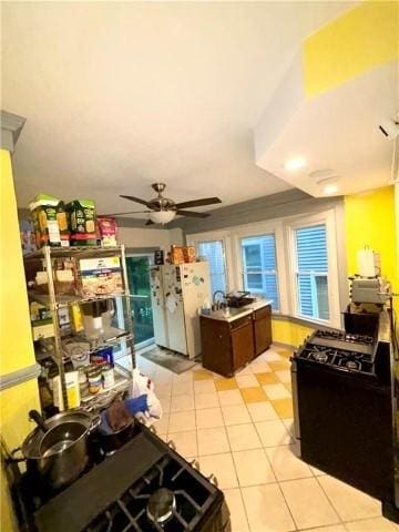 kitchen with black gas stove, light tile patterned floors, white fridge, dark brown cabinetry, and ceiling fan