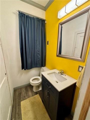 bathroom featuring wood-type flooring, toilet, vanity, and crown molding