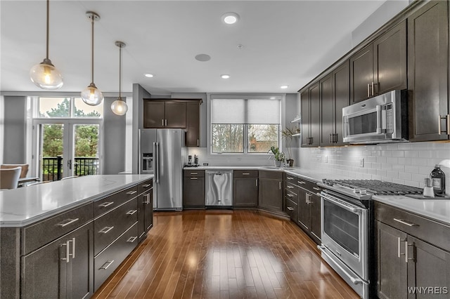 kitchen featuring dark brown cabinets, pendant lighting, dark wood-type flooring, decorative backsplash, and stainless steel appliances