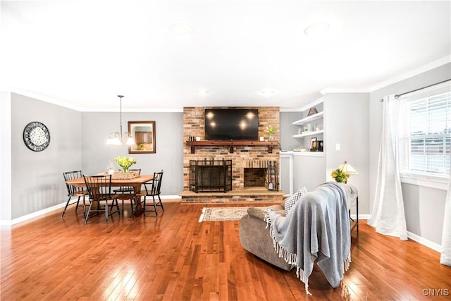 living room with crown molding, hardwood / wood-style flooring, a fireplace, and an inviting chandelier