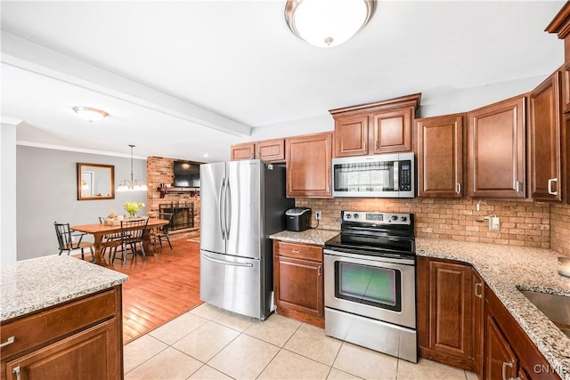 kitchen featuring appliances with stainless steel finishes, hanging light fixtures, decorative backsplash, light stone counters, and light tile patterned flooring