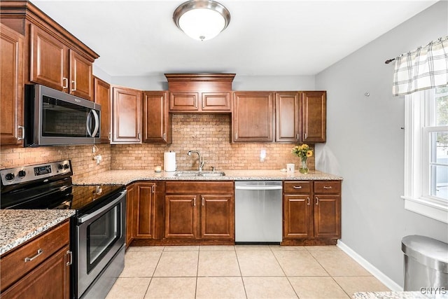 kitchen with sink, tasteful backsplash, light stone countertops, light tile patterned flooring, and stainless steel appliances