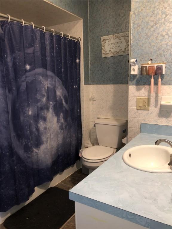 bathroom with toilet, vanity, and tile walls