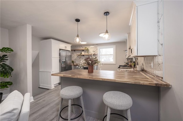 kitchen featuring stainless steel refrigerator with ice dispenser, butcher block counters, a kitchen breakfast bar, kitchen peninsula, and white cabinets