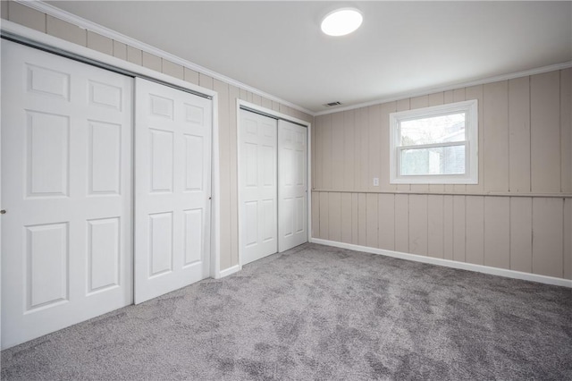 unfurnished bedroom with ornamental molding, light carpet, two closets, and wooden walls