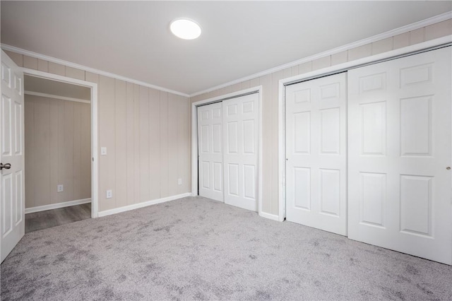 unfurnished bedroom with crown molding, light carpet, and two closets