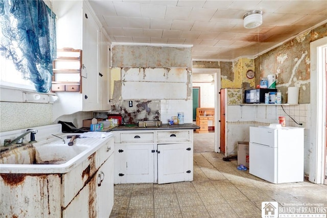 kitchen with white refrigerator, white cabinetry, and sink