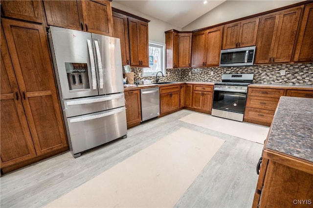 kitchen with appliances with stainless steel finishes, sink, lofted ceiling, and light hardwood / wood-style floors