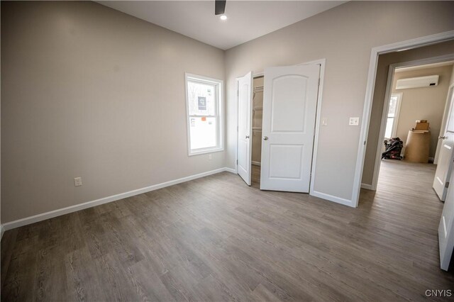 unfurnished bedroom with hardwood / wood-style floors and an AC wall unit