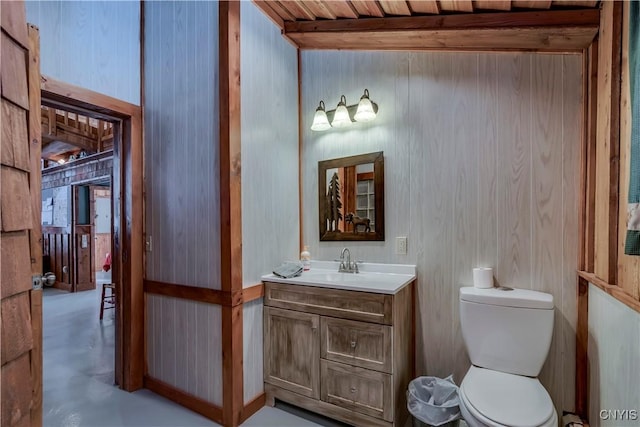 bathroom with concrete flooring, beamed ceiling, vanity, toilet, and wooden ceiling