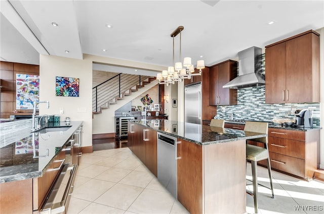 kitchen with light tile patterned flooring, sink, hanging light fixtures, a large island, and wall chimney range hood