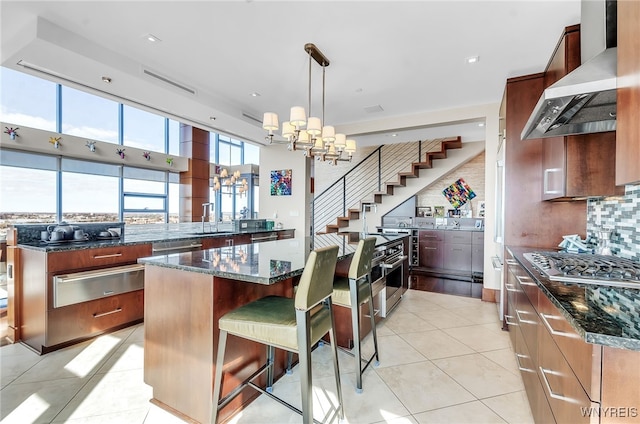 kitchen with a kitchen island, pendant lighting, dark stone countertops, a kitchen breakfast bar, and wall chimney range hood