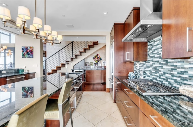 kitchen featuring appliances with stainless steel finishes, pendant lighting, decorative backsplash, dark stone counters, and wall chimney exhaust hood