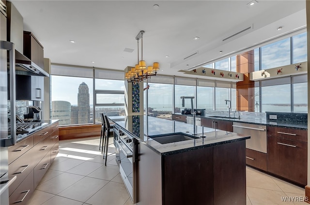 kitchen featuring sink, dark stone countertops, hanging light fixtures, an island with sink, and light tile patterned flooring