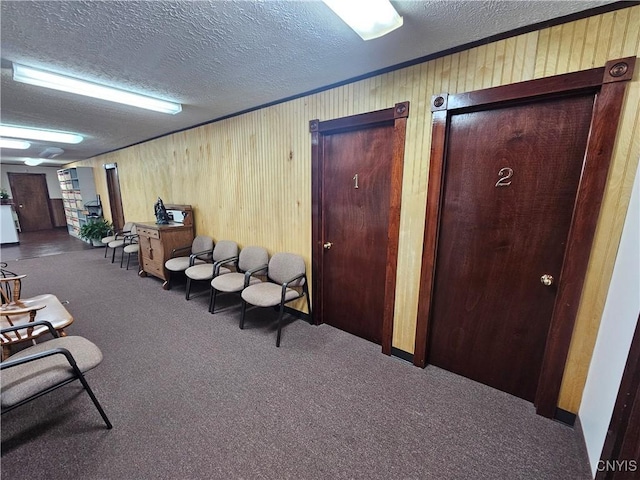 interior space with ornamental molding, dark carpet, a textured ceiling, and wood walls