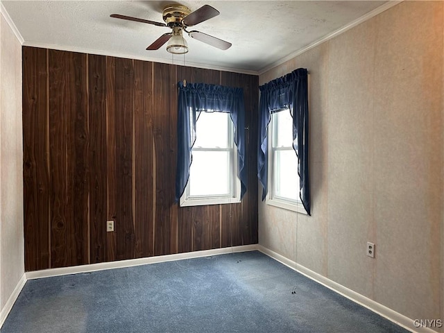 carpeted empty room with ornamental molding, a textured ceiling, ceiling fan, and wooden walls