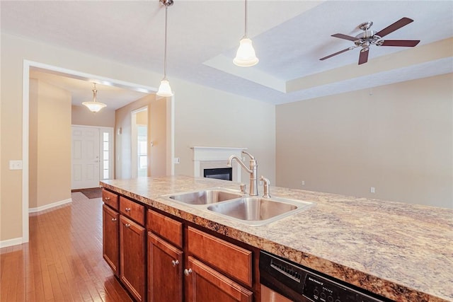 kitchen with hanging light fixtures, sink, dishwashing machine, and light wood-type flooring