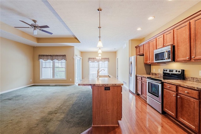 kitchen with sink, appliances with stainless steel finishes, hanging light fixtures, a textured ceiling, and a center island with sink