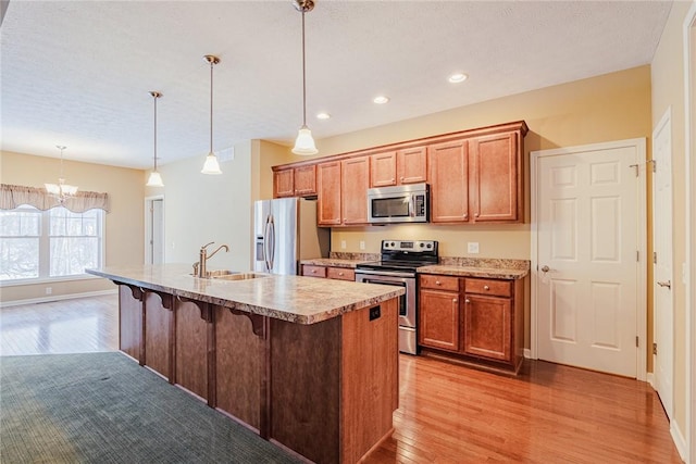 kitchen with sink, a breakfast bar area, hanging light fixtures, stainless steel appliances, and a center island with sink