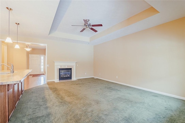 unfurnished living room with a raised ceiling, sink, ceiling fan, and carpet flooring