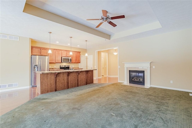 unfurnished living room with carpet floors, ceiling fan, and a tray ceiling