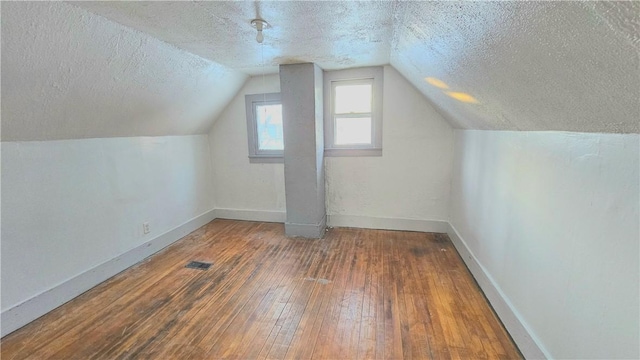 additional living space featuring lofted ceiling, dark hardwood / wood-style flooring, and a textured ceiling