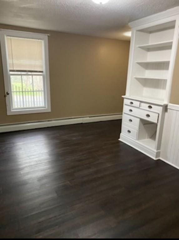 spare room with built in shelves, dark hardwood / wood-style flooring, a textured ceiling, and a baseboard heating unit