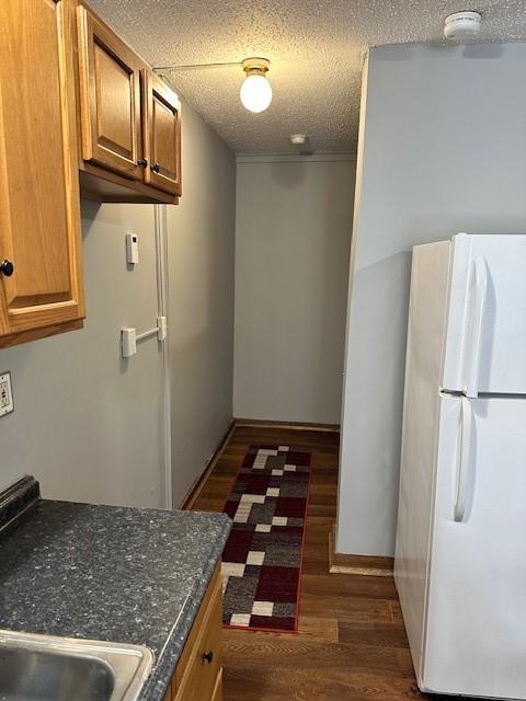 kitchen with white fridge, dark wood-type flooring, and a textured ceiling