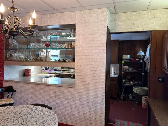 kitchen with range with electric cooktop, brick wall, pendant lighting, a paneled ceiling, and an inviting chandelier