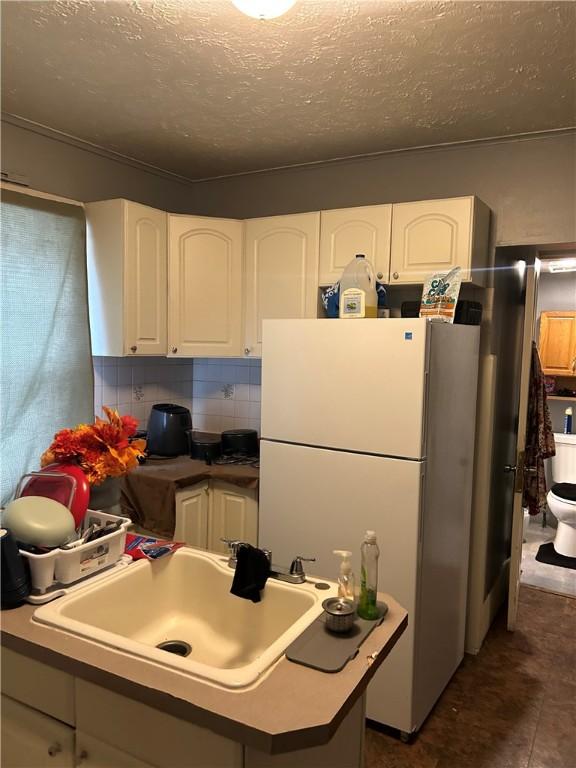 kitchen with tasteful backsplash, sink, white cabinets, white refrigerator, and a textured ceiling