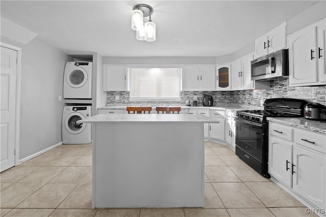 kitchen with stacked washing maching and dryer, a center island, white cabinets, and black gas range