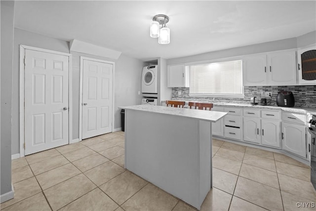 kitchen featuring white cabinetry, a center island, light tile patterned floors, stacked washer / dryer, and backsplash