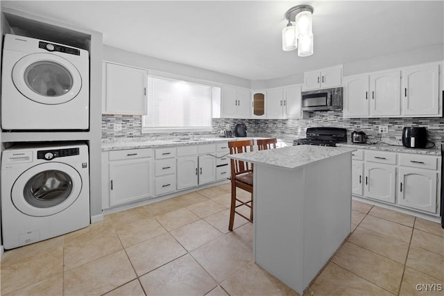 kitchen featuring stacked washer / drying machine, range, a center island, and white cabinets