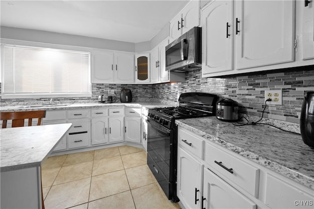 kitchen featuring light tile patterned flooring, black gas stove, white cabinets, and backsplash