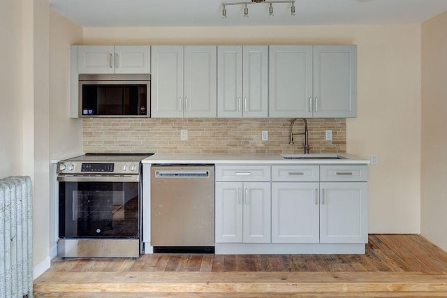 kitchen featuring sink, radiator, stainless steel appliances, decorative backsplash, and light wood-type flooring