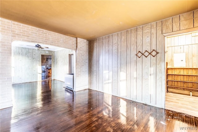 unfurnished room with ceiling fan, brick wall, wood-type flooring, and wooden walls