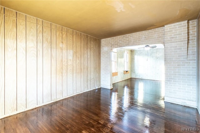 spare room with ceiling fan, dark hardwood / wood-style flooring, and wood walls