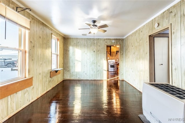 unfurnished living room with dark wood-type flooring, ceiling fan, wooden walls, heating unit, and ornamental molding